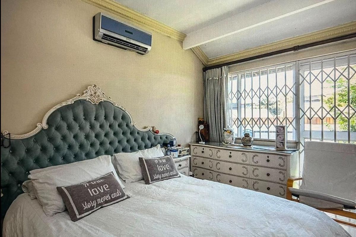 A bedroom featuring a vaulted ceiling, crown molding, a wall-mounted air conditioning unit, and a window fitted with a security gate.