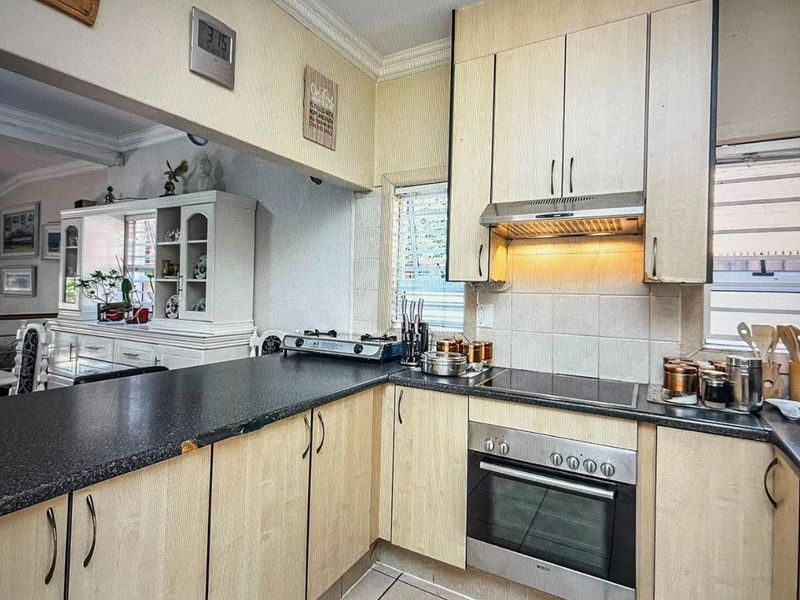 A functional kitchen featuring light wood-finish cabinetry, dark laminate countertops, built-in oven, and an integrated extractor fan with tiled backsplash.