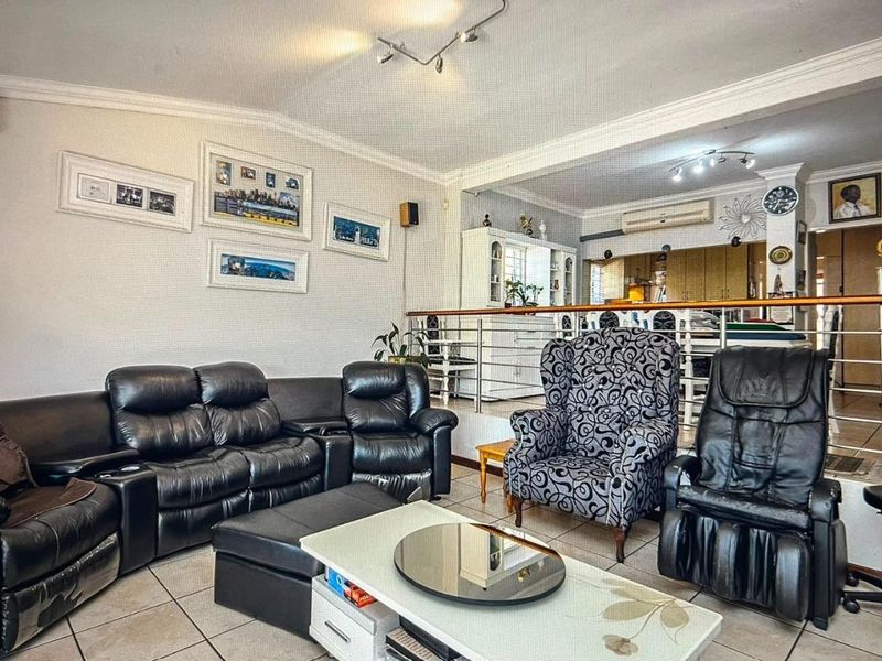 Open-plan living area featuring tiled flooring, split-system air conditioning, and a raised dining section separated by a modern stainless steel balustrade.