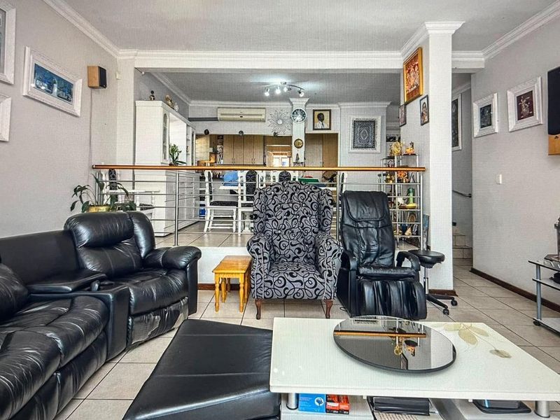 An open-plan living area featuring tiled flooring, crown molding, and a raised dining section separated by a stainless steel balustrade.