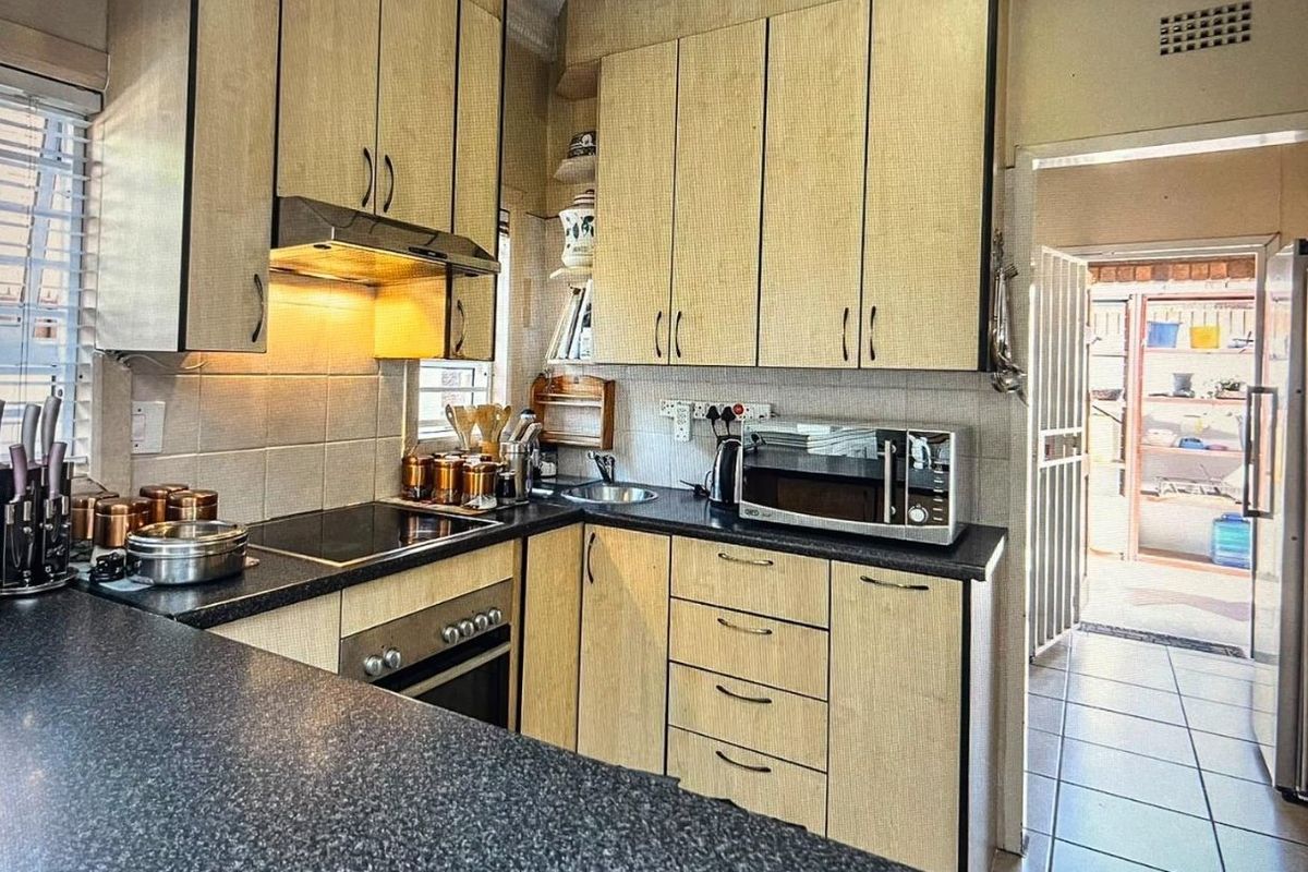 A functional kitchen featuring light-toned laminate cabinetry, dark countertops, an integrated electric hob, built-in oven, and tiled flooring with direct access to an outdoor area.