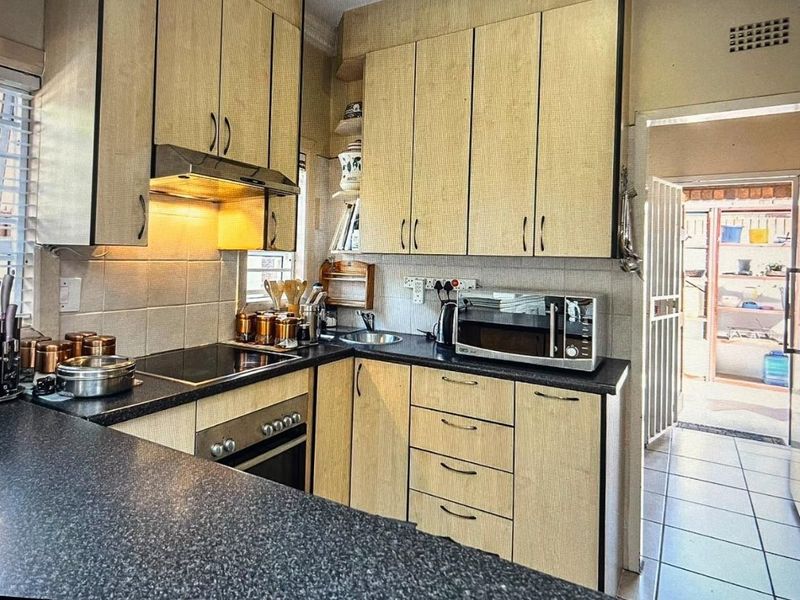A functional kitchen featuring light-toned laminate cabinetry, dark countertops, an integrated electric hob, built-in oven, and tiled flooring with direct access to an outdoor area.