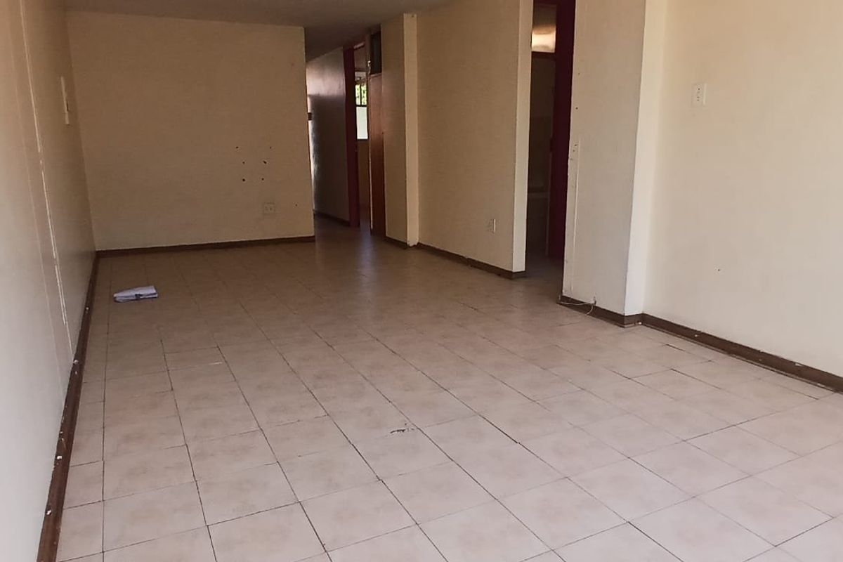 An empty, open-plan living area featuring tiled flooring and neutral walls, offering a blank canvas for renovation or interior design updates.