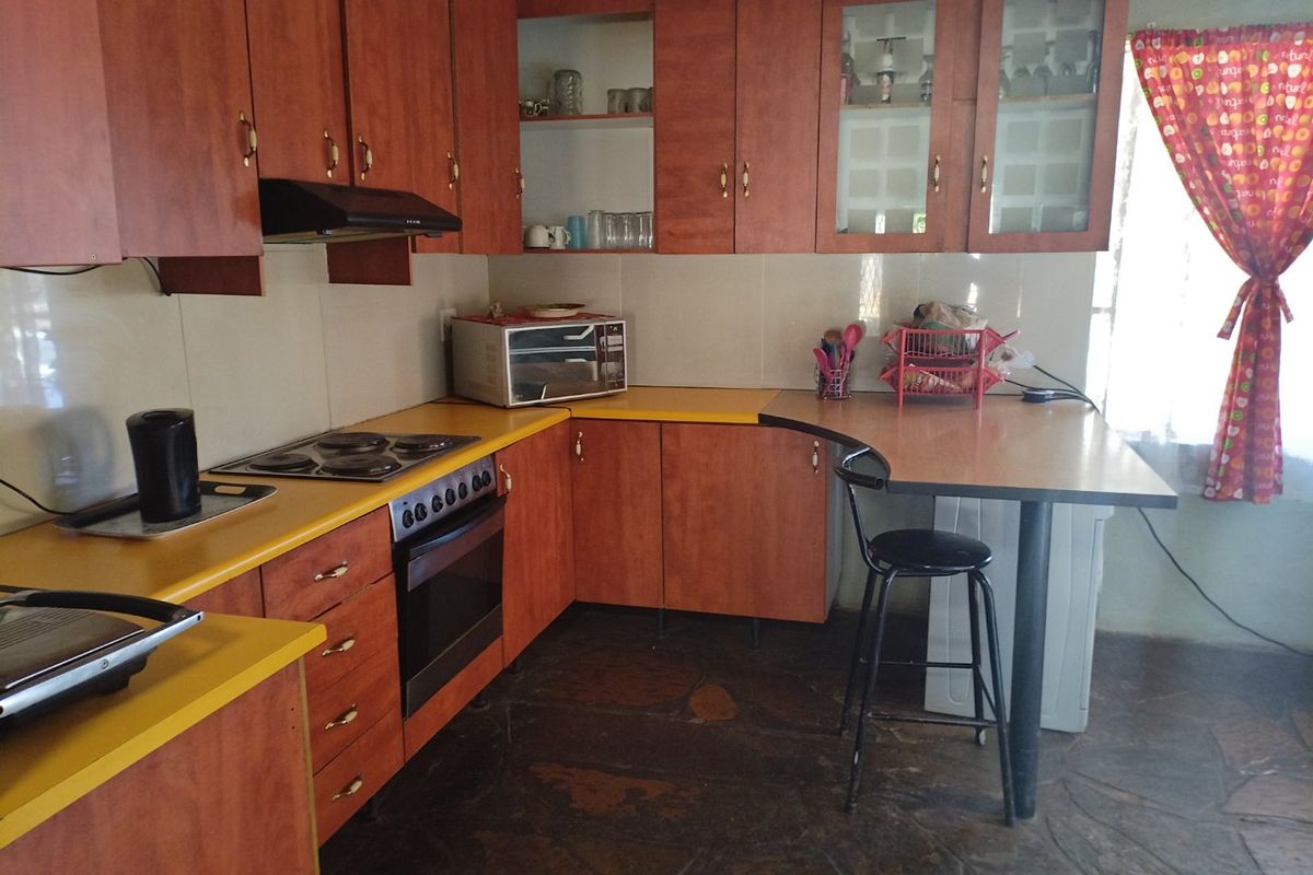 A dated kitchen featuring wood-look laminate cabinetry, yellow countertops, built-in oven, electric hob, and stone flooring.