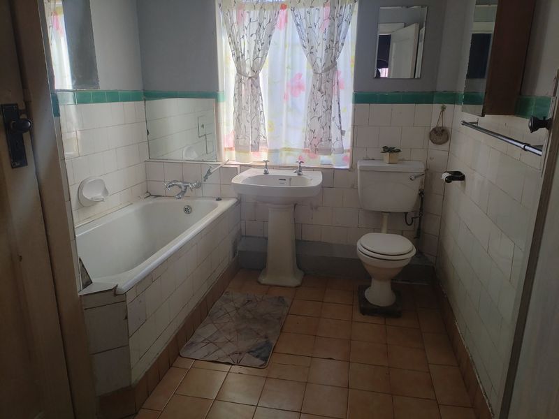 A dated bathroom featuring a pedestal basin, bathtub, and toilet with original ceramic tiling, offering significant potential for a modern renovation.