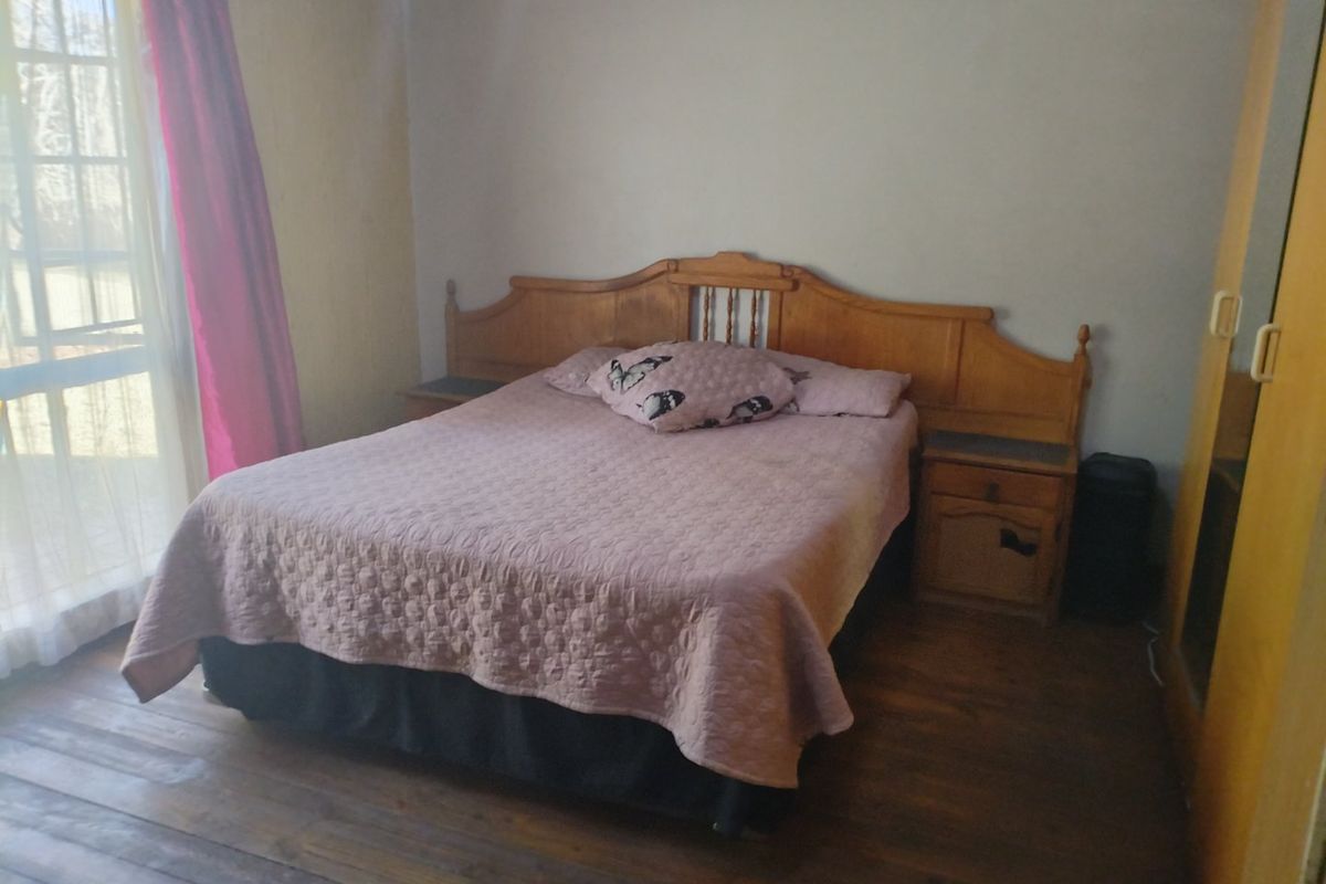 A bedroom featuring timber flooring, a built-in wardrobe, and an air conditioning unit, with access to natural light through a sliding glass door.