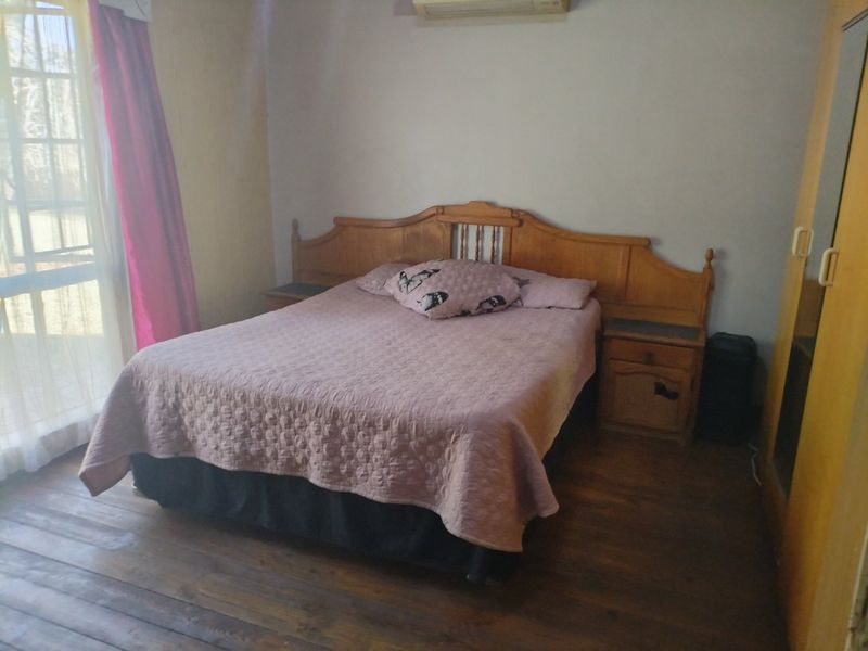 A bedroom featuring timber flooring, a built-in wardrobe, and an air conditioning unit, with access to natural light through a sliding glass door.