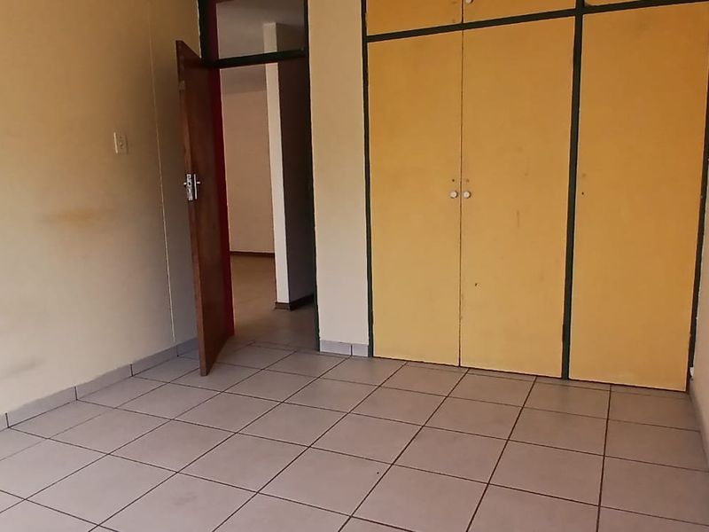 An empty bedroom featuring tiled flooring and built-in cupboards, requiring cosmetic updates to improve its overall appeal.