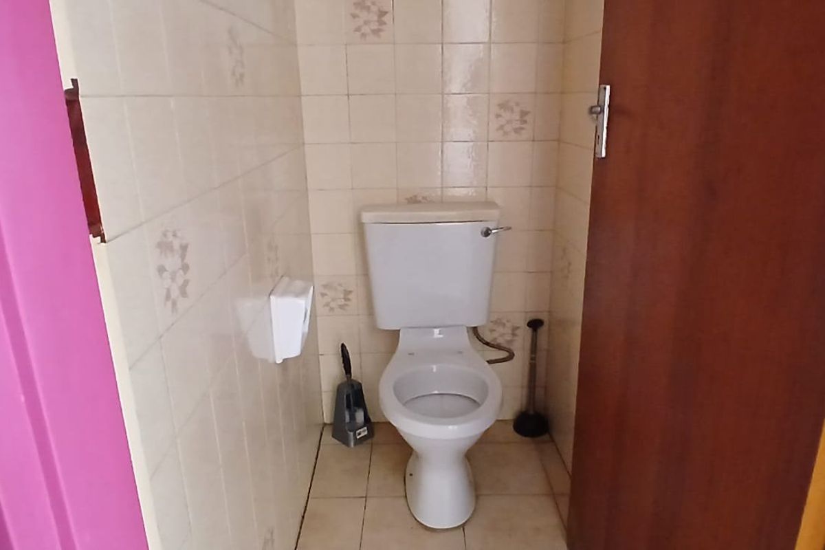 A compact bathroom featuring a standard toilet, tiled walls, and tiled flooring, currently in need of cosmetic updates and minor tile repairs.