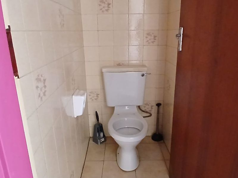 A compact bathroom featuring a standard toilet, tiled walls, and tiled flooring, currently in need of cosmetic updates and minor tile repairs.