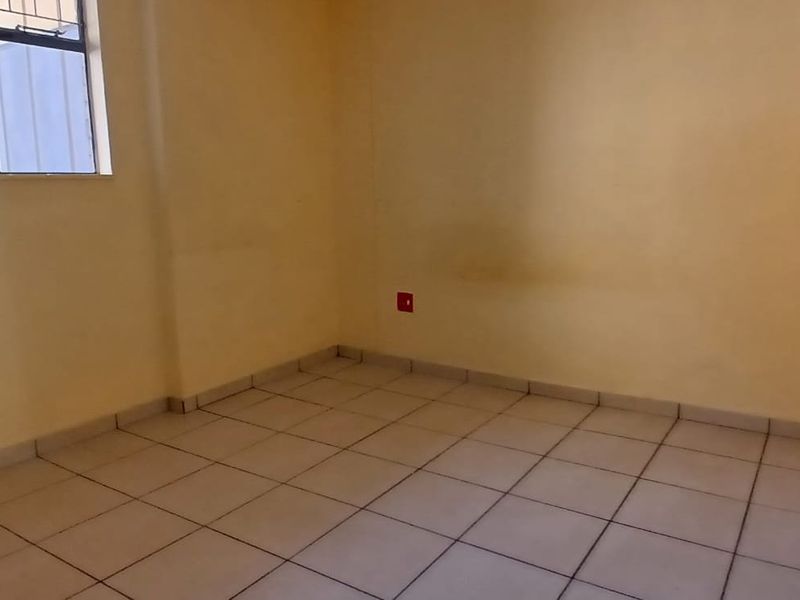 An empty bedroom featuring tiled flooring and a window with security bars, ready for a fresh coat of paint and new finishes.