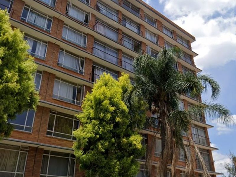 A multi-story brick apartment building featuring private balconies, secure perimeter fencing, and razor wire for added security.