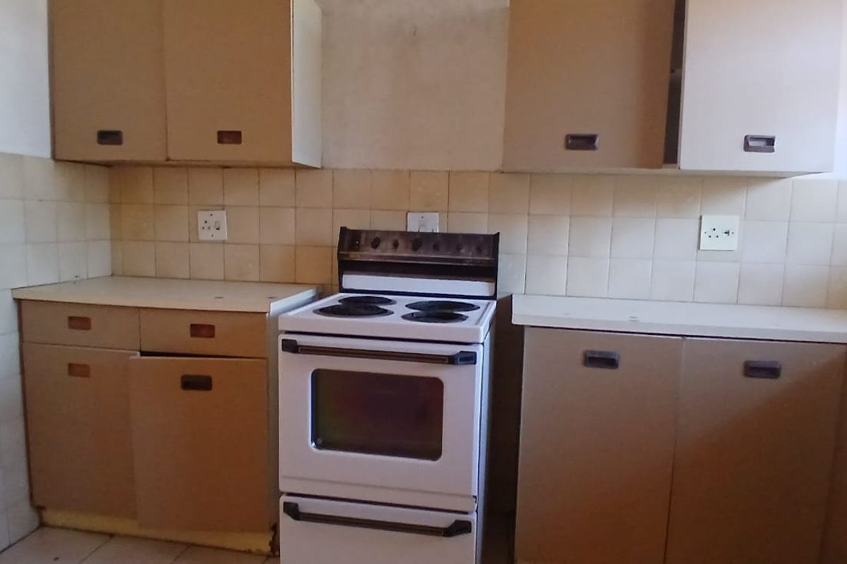 A dated kitchen featuring original cabinetry, tiled backsplash, and a freestanding electric stove, offering significant potential for modernization and renovation.