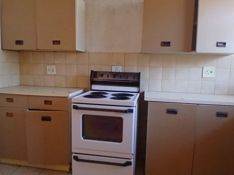 A dated kitchen featuring original cabinetry, tiled backsplash, and a freestanding electric stove, offering significant potential for modernization and renovation.