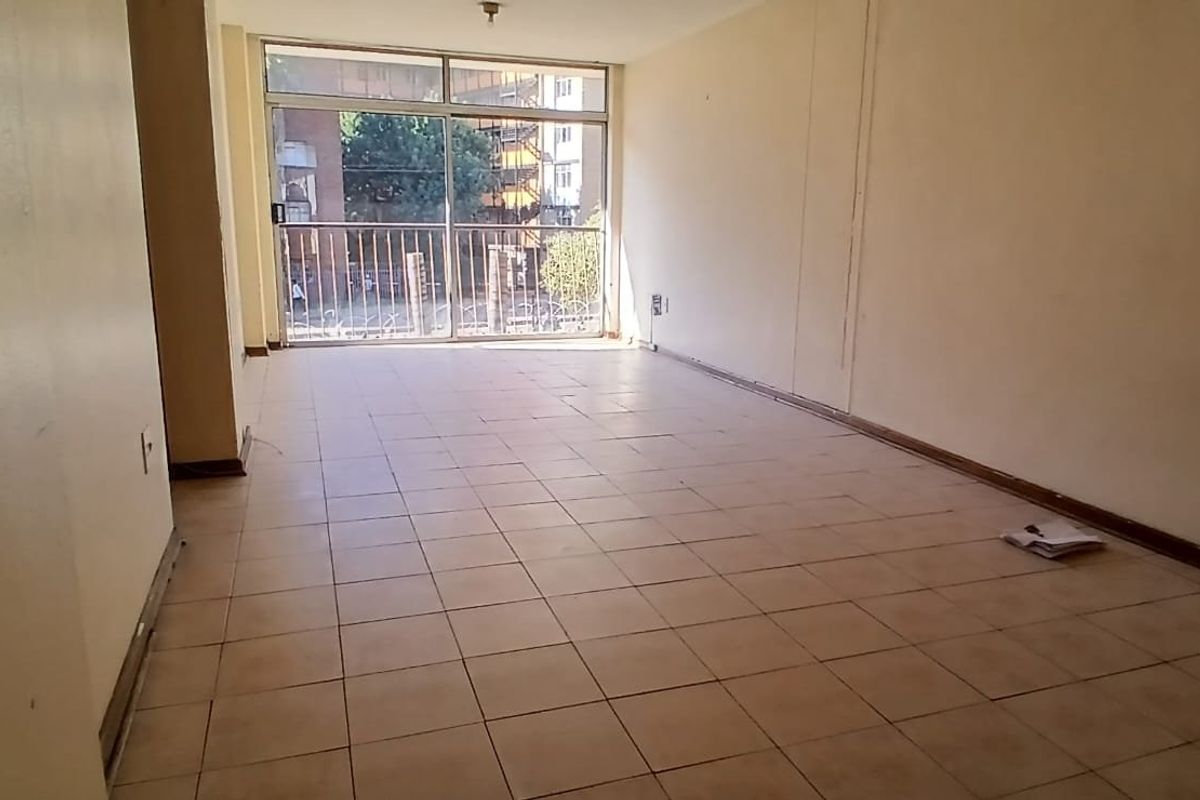 An empty, open-plan living area featuring tiled flooring and a sliding glass door leading to a balcony with security gate.