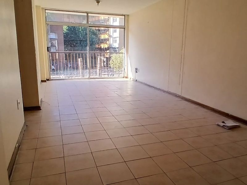 An empty, open-plan living area featuring tiled flooring and a sliding glass door leading to a balcony with security gate.