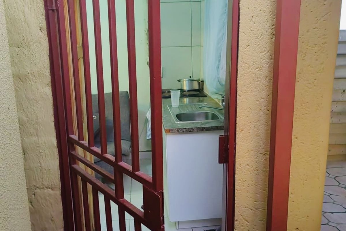 A compact kitchen area viewed through a red security gate, featuring built-in cabinetry, a stainless steel sink, and a built-in hob.