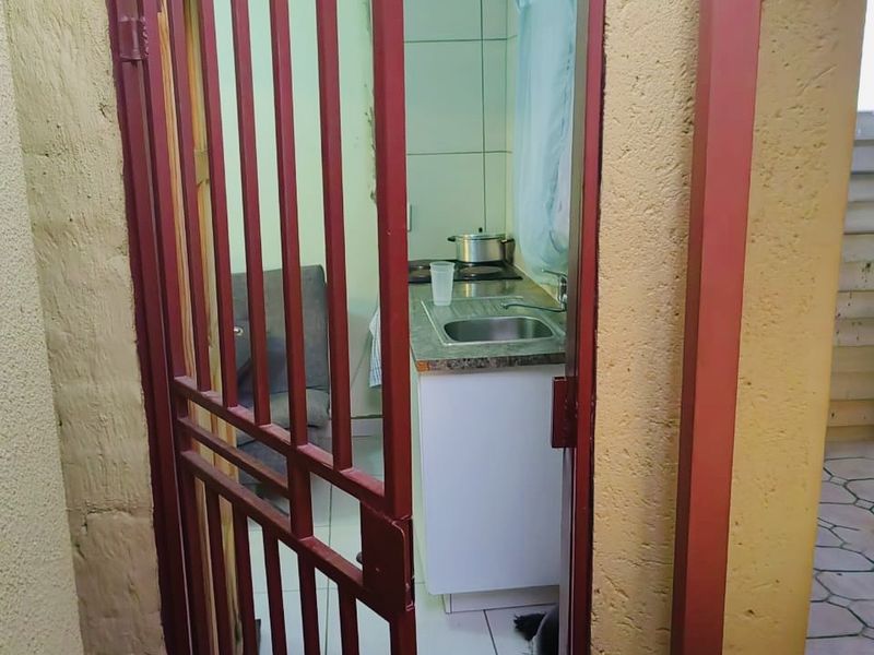 A compact kitchen area viewed through a red security gate, featuring built-in cabinetry, a stainless steel sink, and a built-in hob.