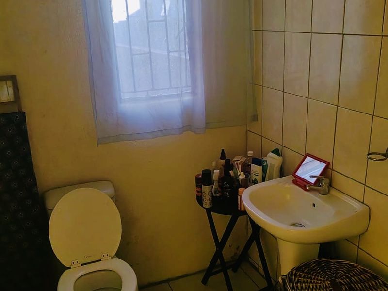 A compact bathroom featuring a pedestal basin, toilet, and tiled wall finishes. The space would benefit from cosmetic updates and improved lighting.