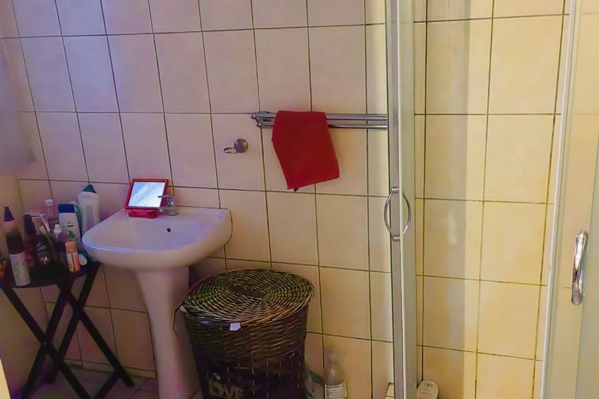 A compact bathroom featuring a pedestal sink and a corner shower enclosure with tiled walls and flooring.