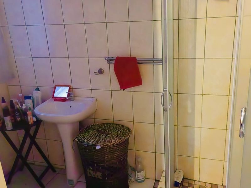 A compact bathroom featuring a pedestal sink and a corner shower enclosure with tiled walls and flooring.