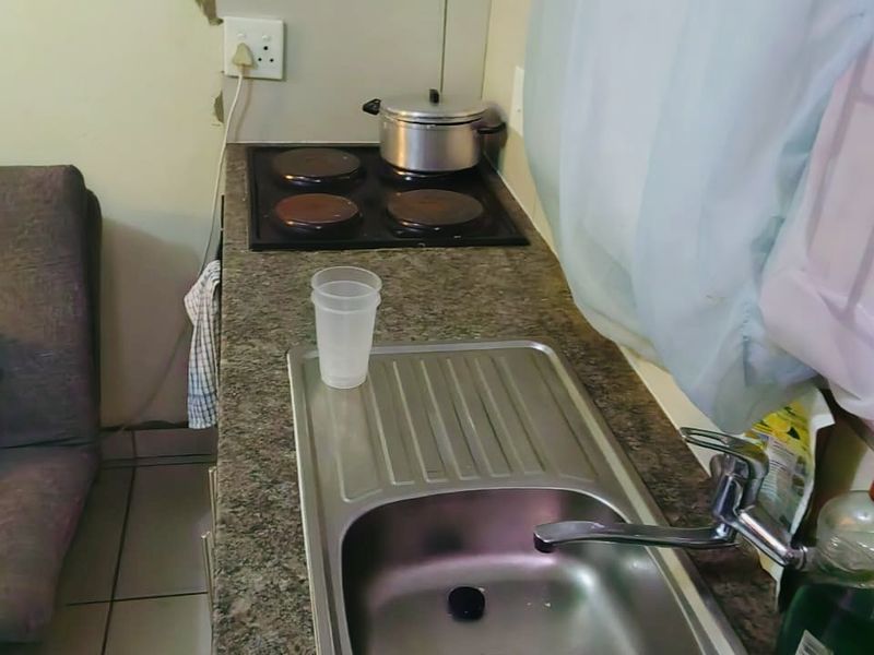 A compact kitchen area featuring a stainless steel sink, granite countertop, and built-in electric hob with visible wall damage requiring repair.