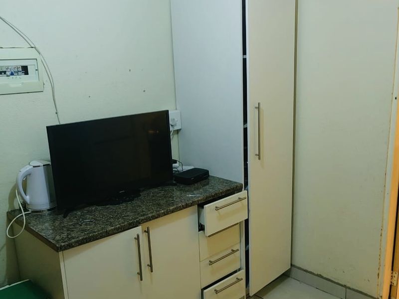 A bedroom area featuring built-in white cabinetry with granite countertops and tiled flooring, showing signs of wear on the walls and door frame.