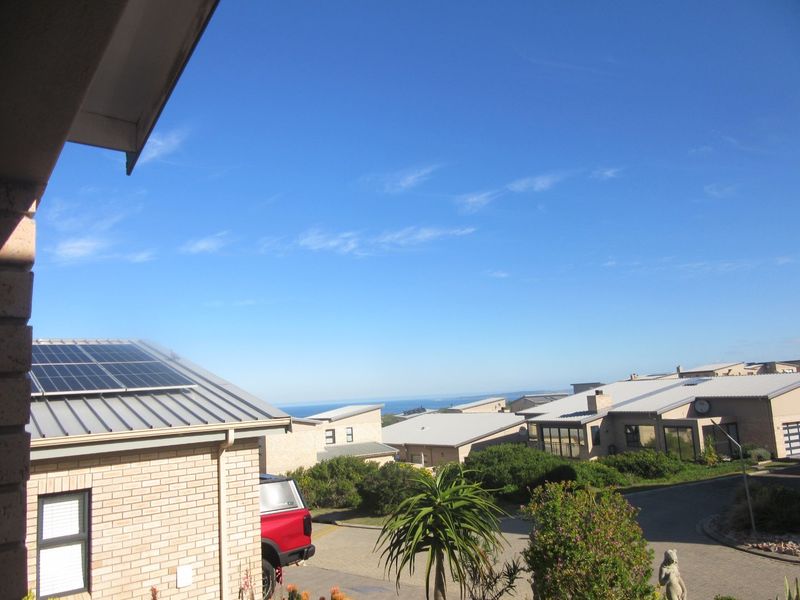 Elevated view overlooking a residential estate with modern brick homes, metal roofing, and solar panel installations under a clear blue sky.