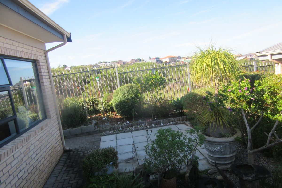 A rear exterior view featuring a paved patio area, brick wall construction, and metal perimeter fencing overlooking the surrounding neighborhood.