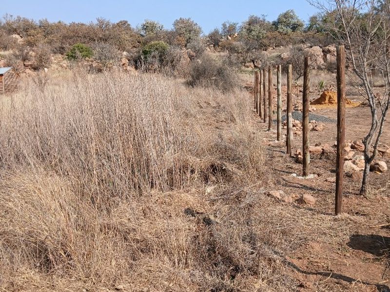 A view of a vacant residential plot featuring natural dry vegetation and a line of installed wooden fence posts.