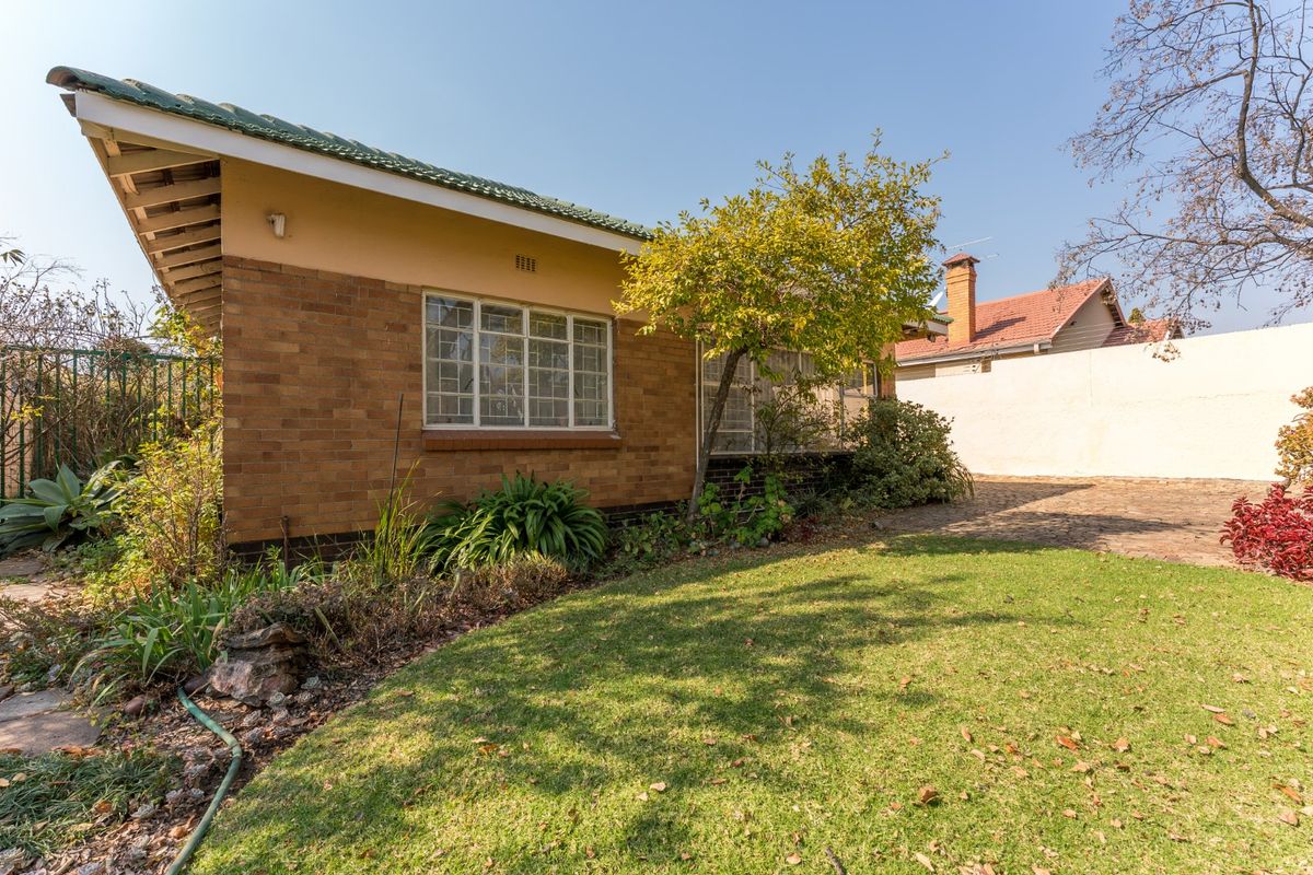 Rear view of a brick-built house featuring a tiled roof, steel-framed windows, and a paved patio area adjacent to a lawn.