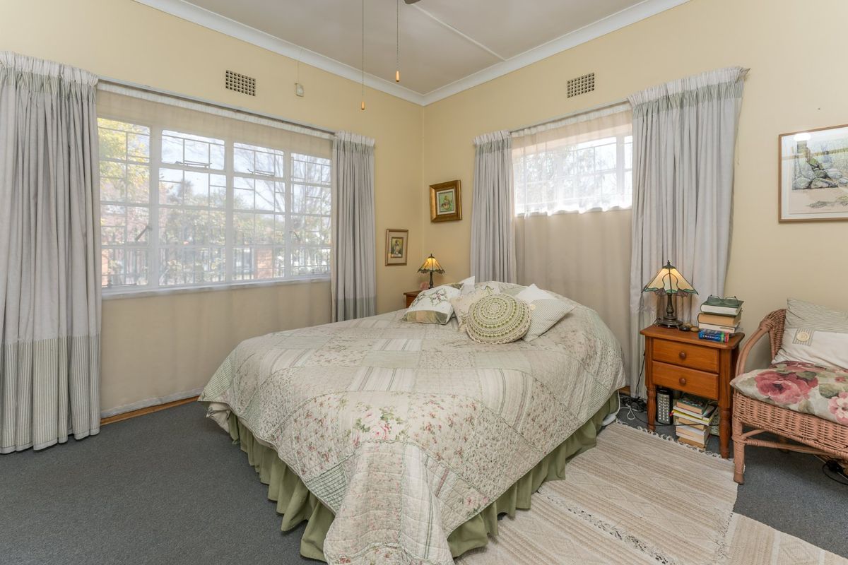 A well-lit bedroom featuring dual aspect windows, ceiling fan, and classic cornice detailing, offering a comfortable and functional living space.