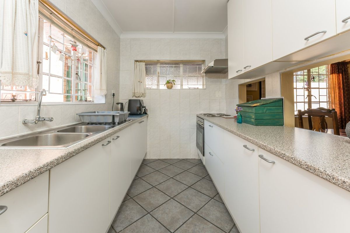 A functional galley-style kitchen featuring white cabinetry, laminate countertops, a built-in oven, cooktop, and tiled finishes throughout.
