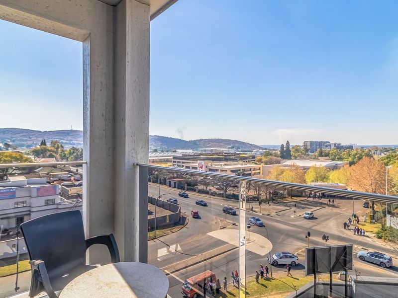 A balcony featuring a modern glass balustrade, offering an elevated view of the surrounding urban landscape and street intersection.