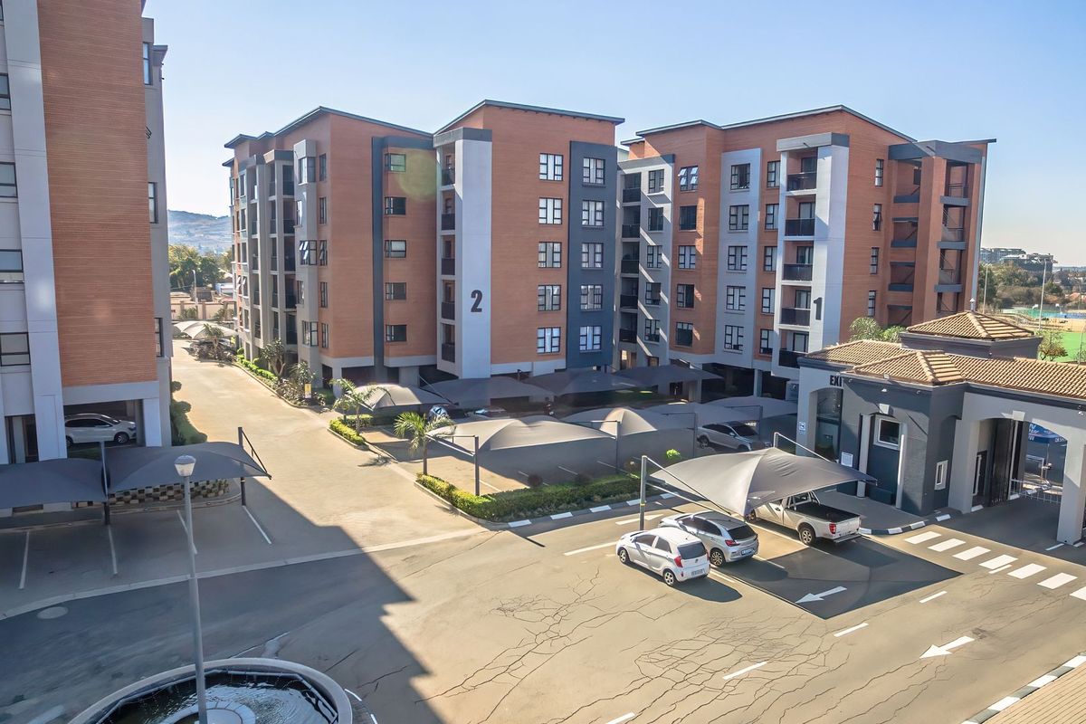 Aerial view of a modern apartment complex featuring brick buildings, covered parking structures, and a secure gated entrance.