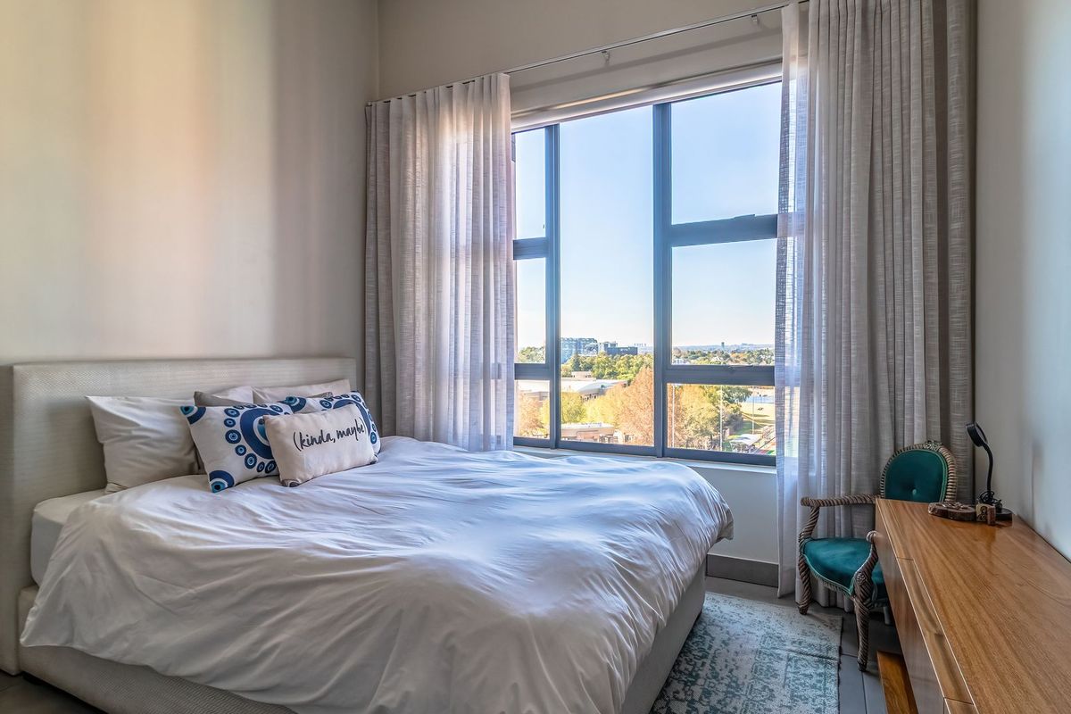 A bright bedroom featuring a large window with natural light, neutral wall finishes, and modern aluminium window frames.