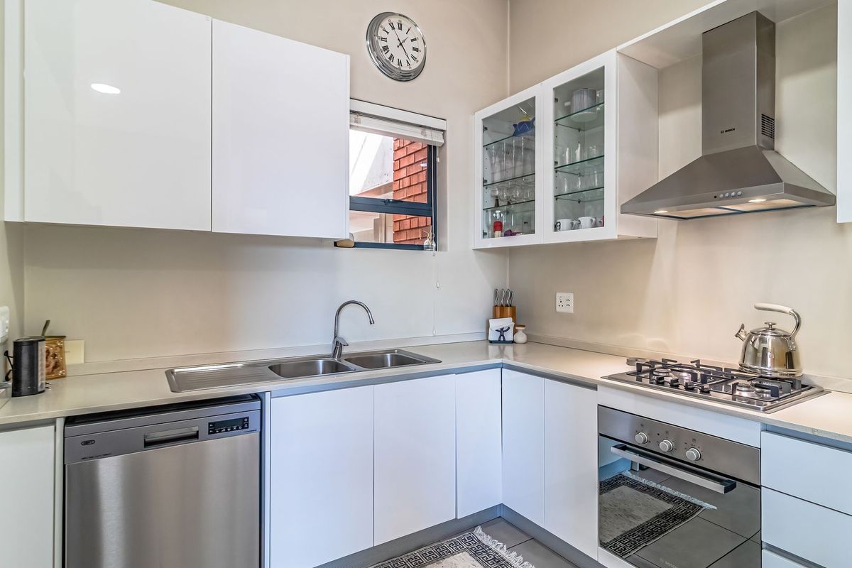 Modern kitchen featuring white cabinetry, stone countertops, stainless steel appliances including a gas hob, oven, extractor fan, and integrated dishwasher.