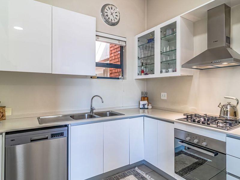Modern kitchen featuring white cabinetry, stone countertops, stainless steel appliances including a gas hob, oven, extractor fan, and integrated dishwasher.