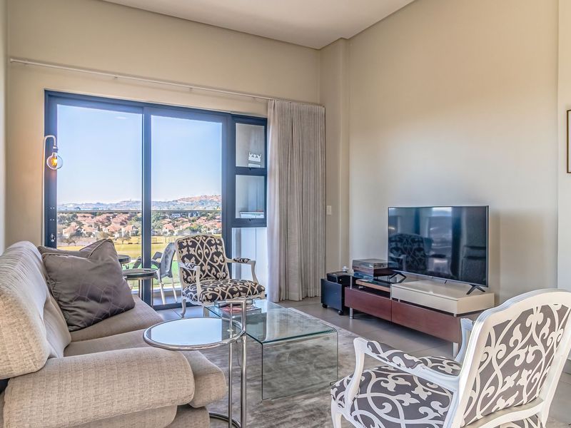 A bright and modern living room featuring large sliding glass doors that open to a balcony with scenic views and neutral tiled flooring.