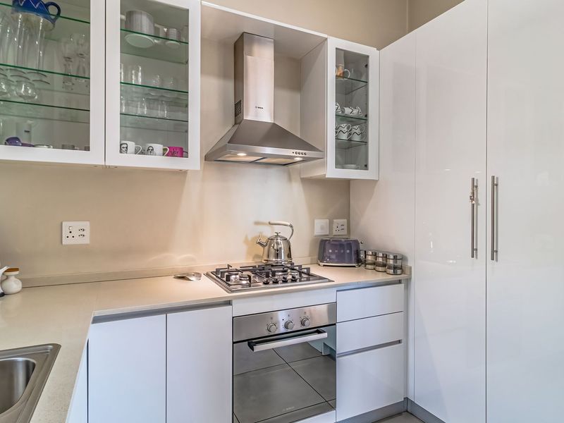 Modern kitchen featuring high-gloss white cabinetry, stone countertops, integrated stainless steel appliances, and glass-fronted display units.