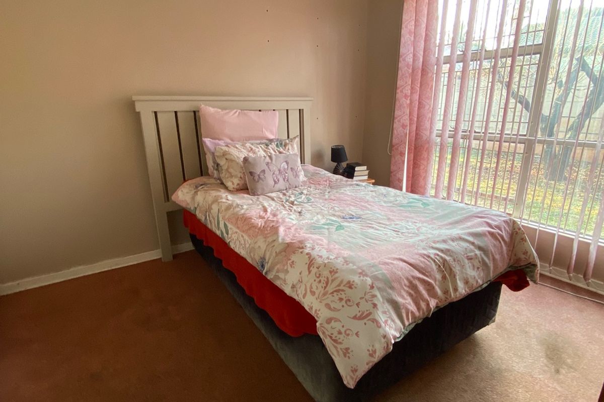 A bedroom featuring carpet flooring, a ceiling fan, and vertical blinds, requiring cosmetic updates to improve the overall condition of the space.