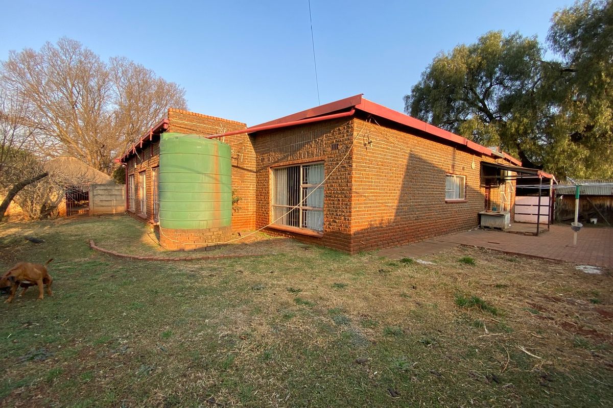 Rear view of a face brick house featuring a water storage tank, paved patio area, and established garden space.