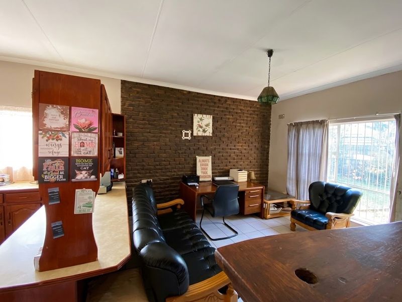 Open plan living area featuring an exposed brick feature wall, tiled flooring, and built-in cabinetry, offering a versatile space for living or home office use.