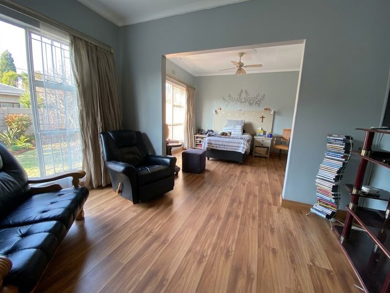 A spacious bedroom featuring laminate flooring, a ceiling fan, and large windows with security bars, offering a bright and functional living space.