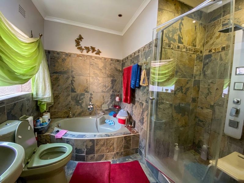 A bathroom featuring a corner bathtub, a separate shower enclosure with a wall-mounted panel, a toilet, and a basin, finished with decorative wall tiling.