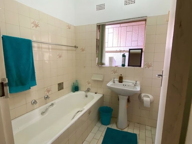 A dated bathroom featuring a pedestal basin, built-in bathtub, and original wall and floor tiling, offering potential for a modern renovation.