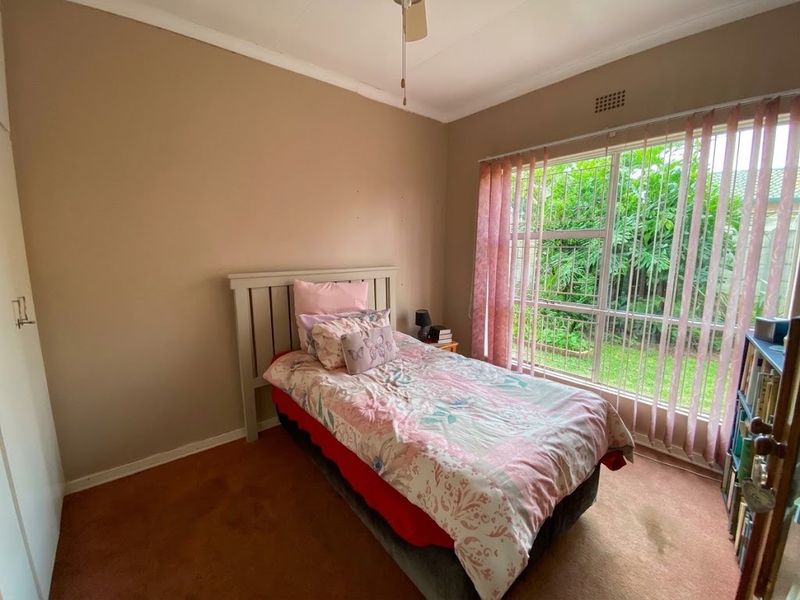 A standard bedroom featuring a large window with security bars, a ceiling fan, and built-in cupboard storage.