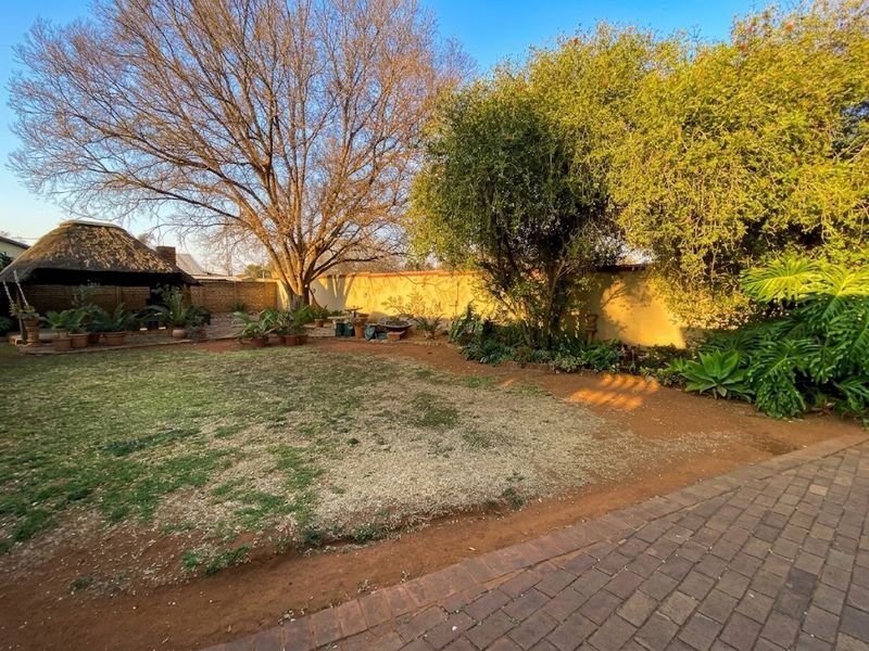 Spacious garden area featuring a thatched lapa, perimeter walling, and established trees, providing a private outdoor space.