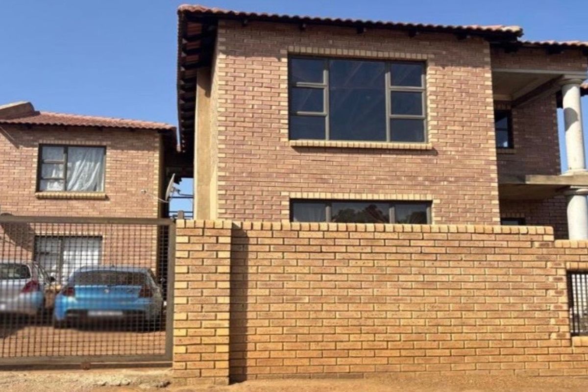 A two-story face-brick residential house featuring a tiled roof, perimeter wall, and a secure metal driveway gate.