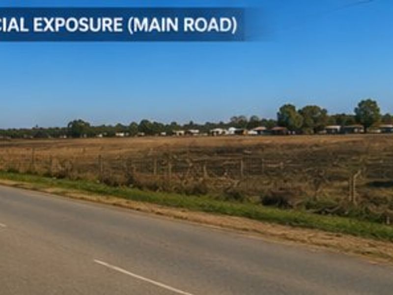 A view of the property frontage along a main road, highlighting commercial exposure potential with existing wire fencing and utility infrastructure.